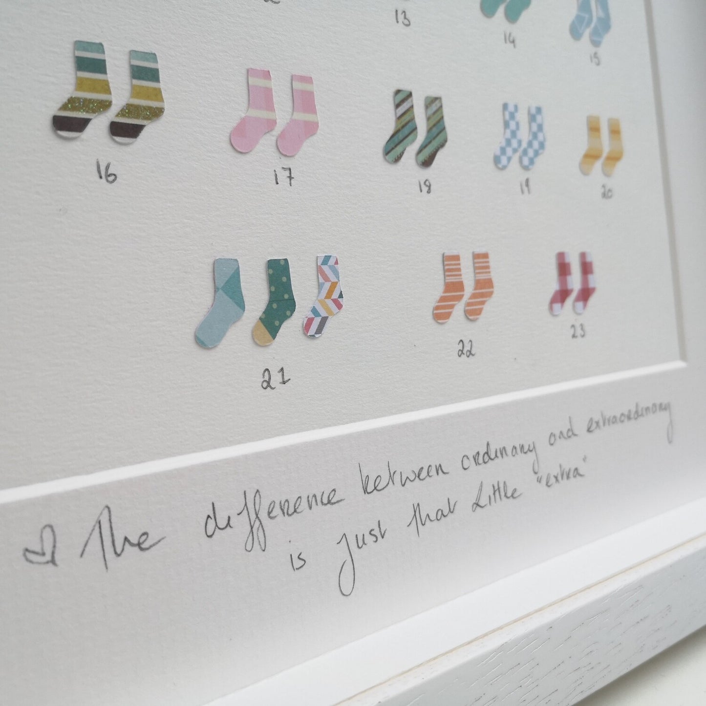 A close up of the 47 papercut socks in a handmade 30x30cm deep box wooden frame, celebrating the 47 chromosomes that people with Down Syndrome have.