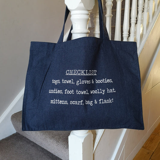 A midnight blue organic cotton tote with toggle closing with the following text on the front in white type font - a personalised checklist so you won't forget to pack anything for swimming! 