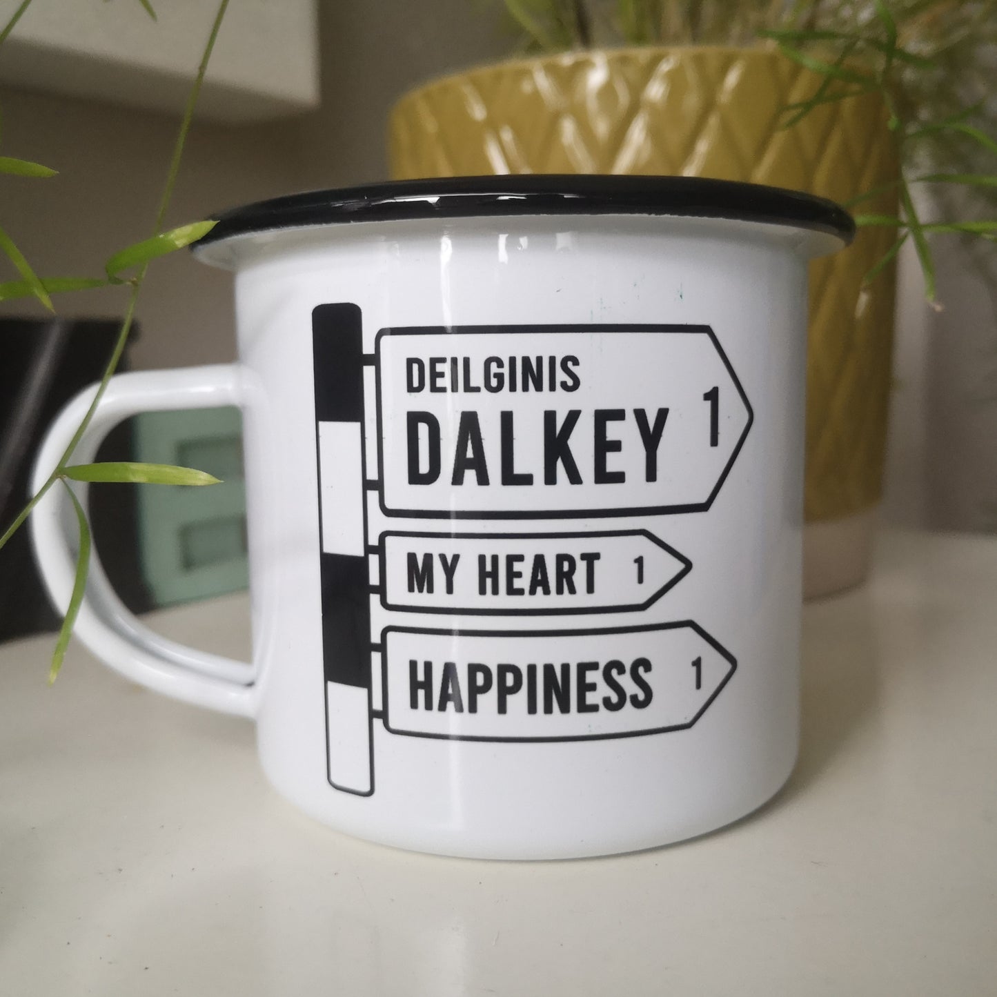 A Customised white steel enamel mug with your selected placename on it in an old fashioned black and white irish roadsign