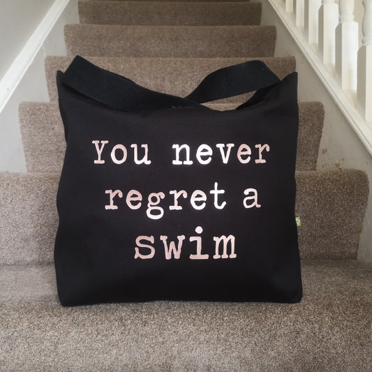 A black organic cotton tote with toggle closing with the following text on the front in white type font - you never regret a swim