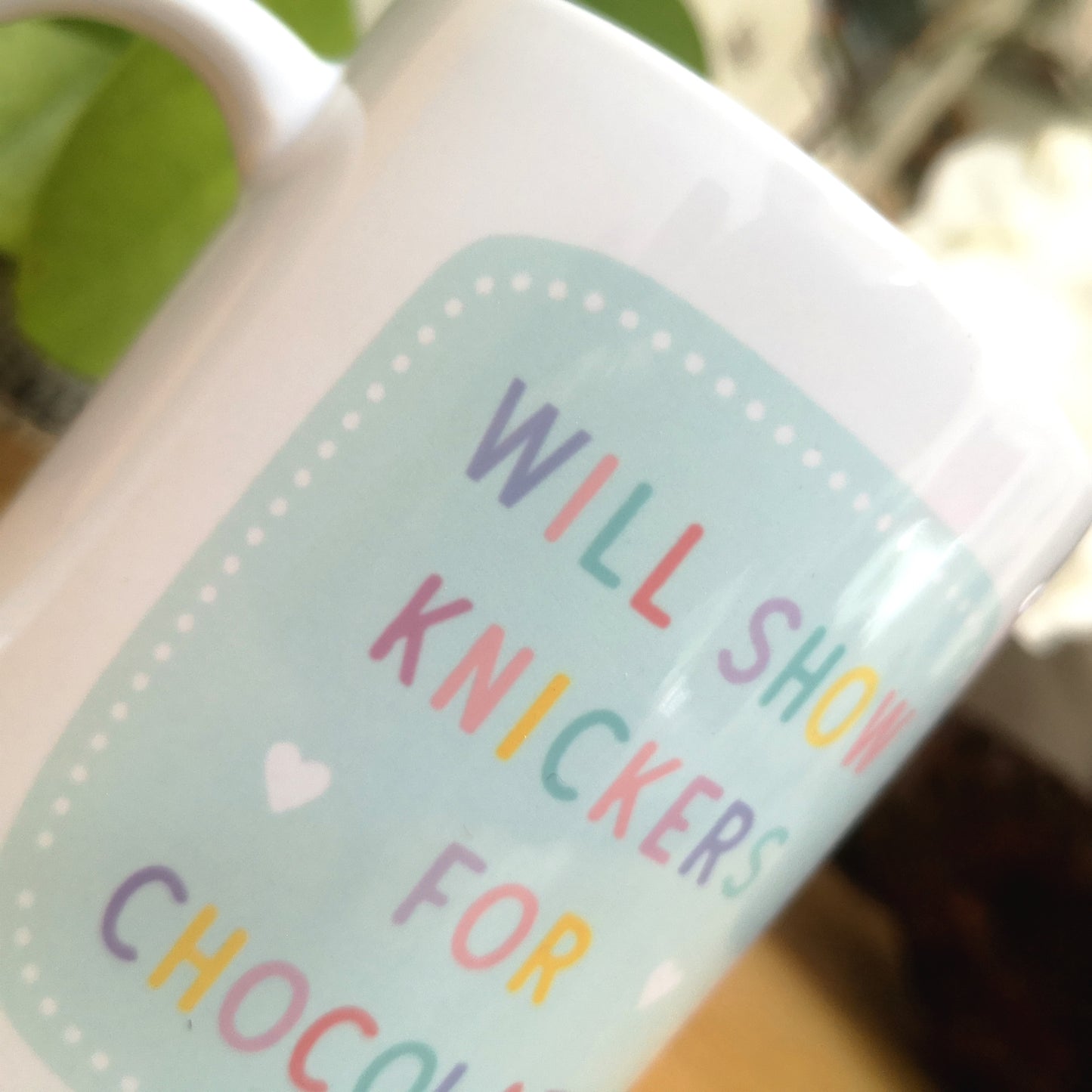 A close up of A ceramic mug with 'WILL SHOW KNICKERS FOR CHOCOLATE' in colourful writing.