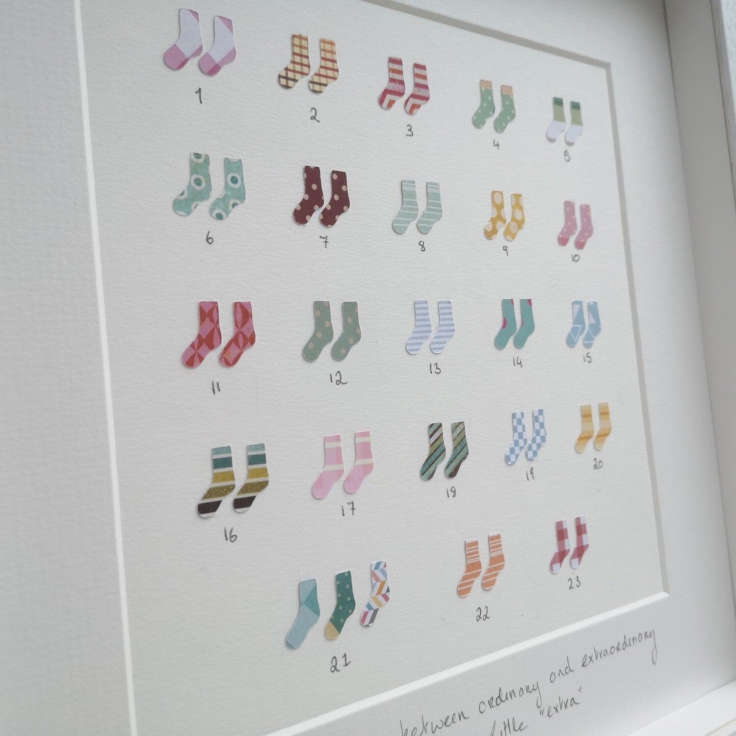 A close up of the 47 papercut socks in a handmade 30x30cm deep box wooden frame, celebrating the 47 chromosomes that people with Down Syndrome have.