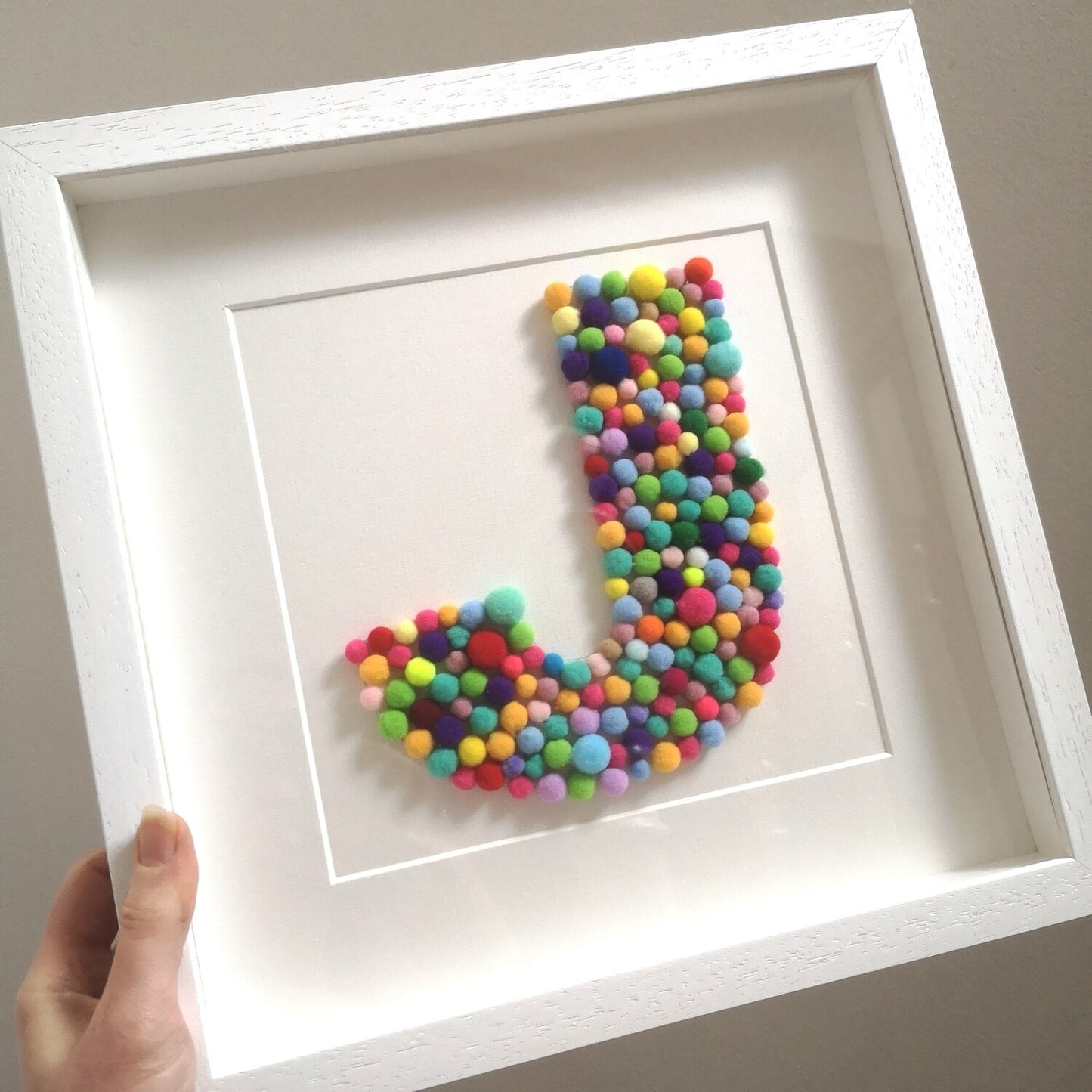 A colourful tactile rainbow pompom Initial frame, in the larger 30x30cm handmade wooden deep box frame