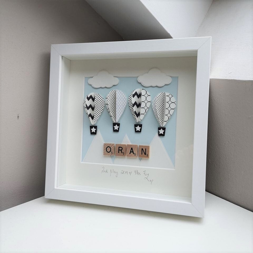 4 black & white patterned papercut balloons on a blue sky and mountain background in a handmade 25x25cm deep box wooden frame.