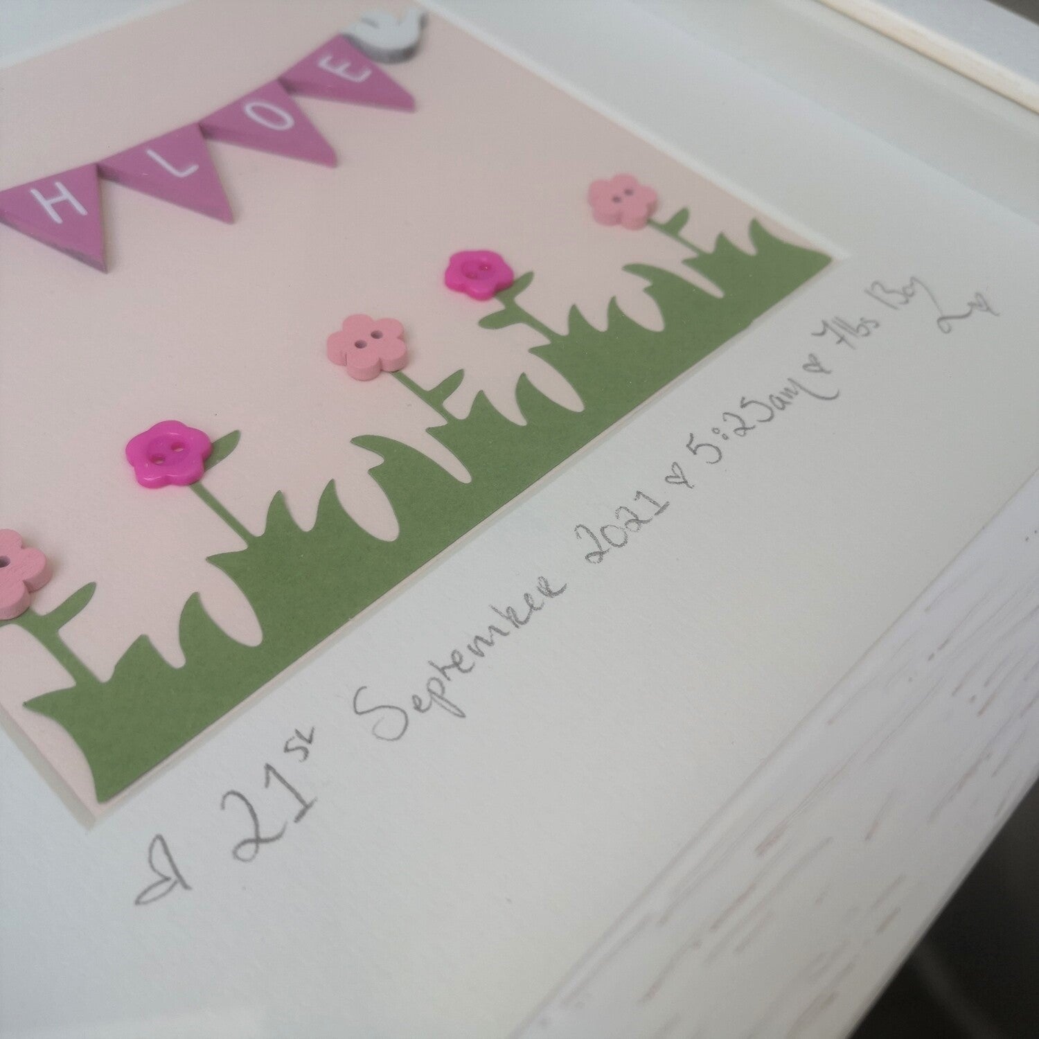 Hand-painted pink wooden bunting and doves, over papercut flowers embellished with buttons, on a pastel pink background,  in a handmade 25x25cm deep box wooden frame.
