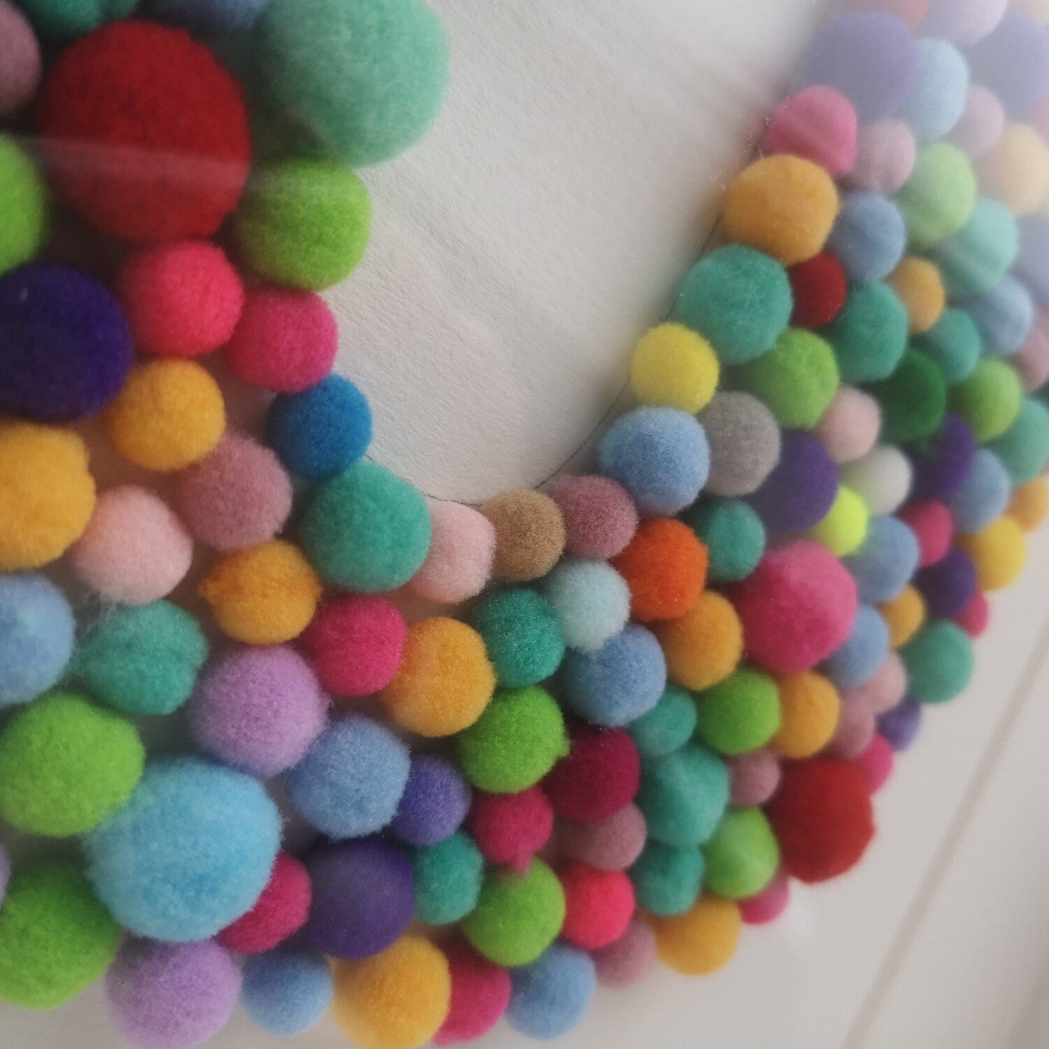 Close up photo of the colourful tactile rainbow pompom Initial frame, in a handmade wooden deep box frame