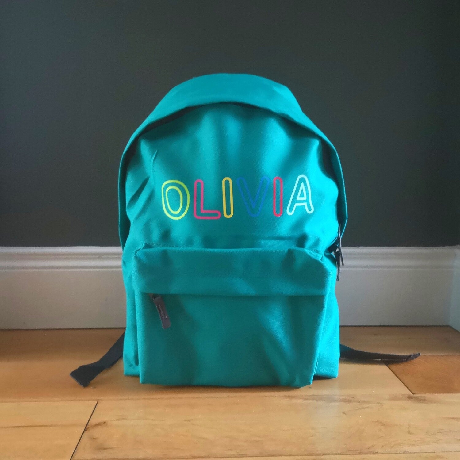 An emerald green kids backpack with their name written along the top in different coloured letters