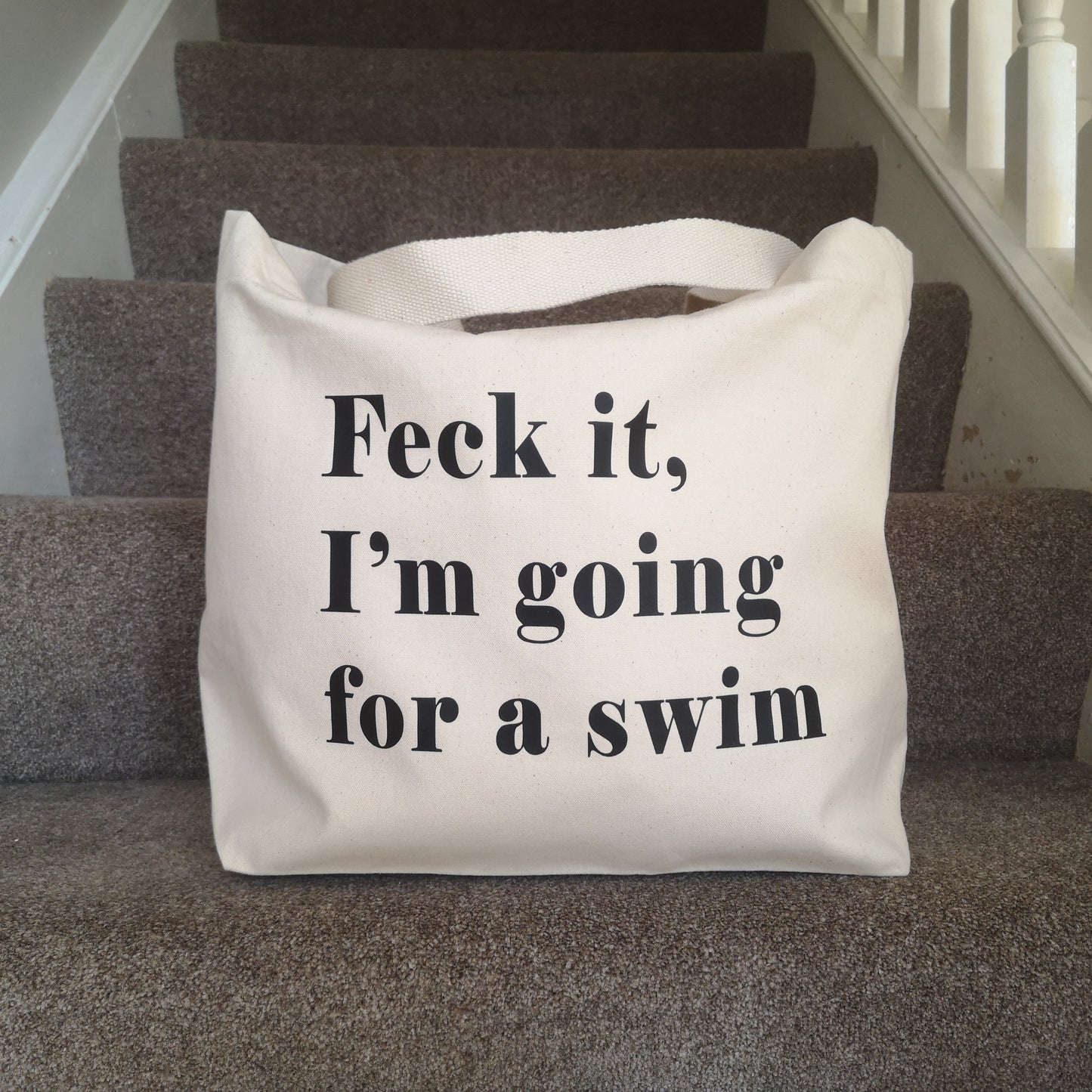 A natural cream organic cotton tote with toggle closing with the following text on the front in black type font - FECK IT, I'M GOING FOR A SWIM