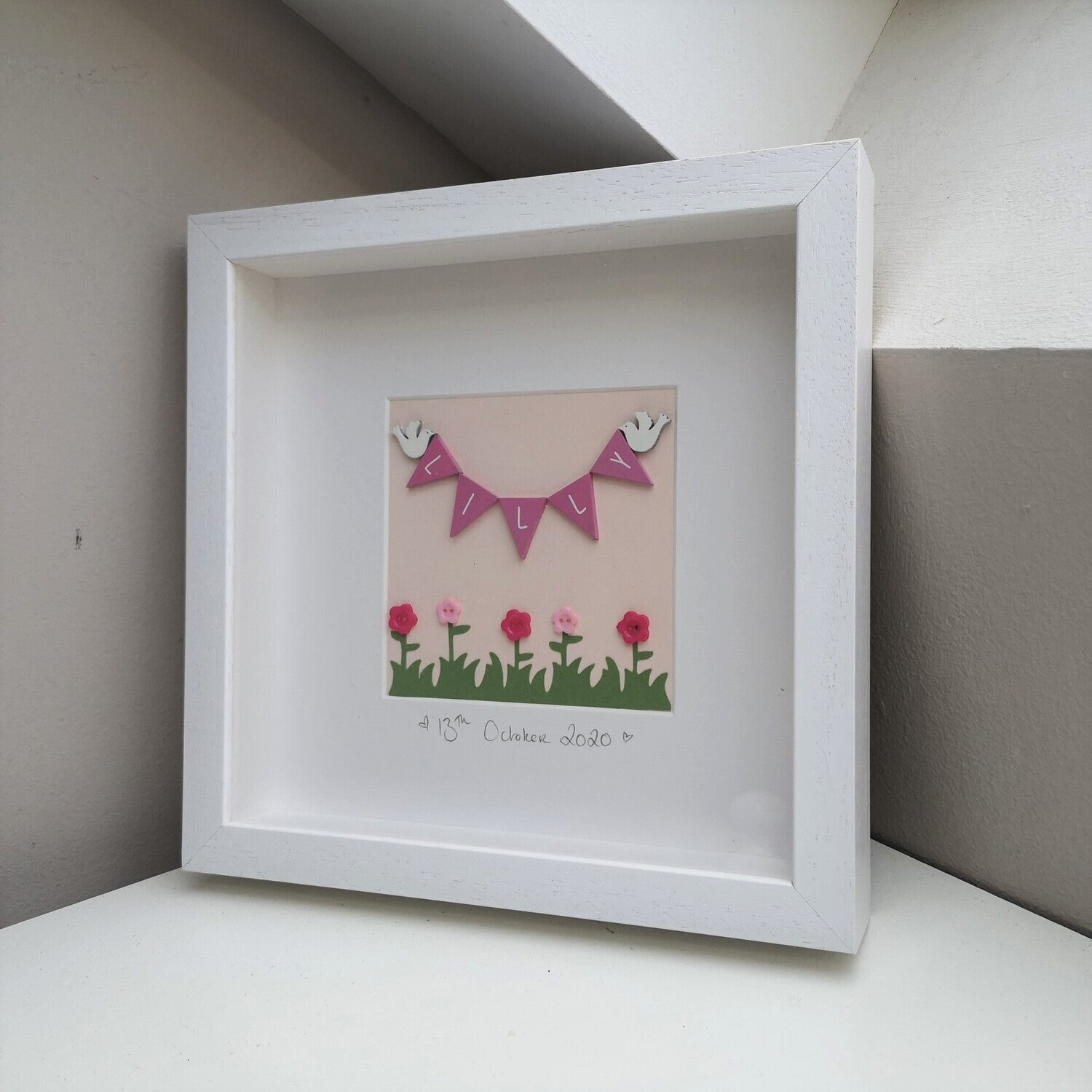 Hand-painted pink wooden bunting and doves, over papercut flowers embellished with buttons, on a pastel pink background,  in a handmade 25x25cm deep box wooden frame.