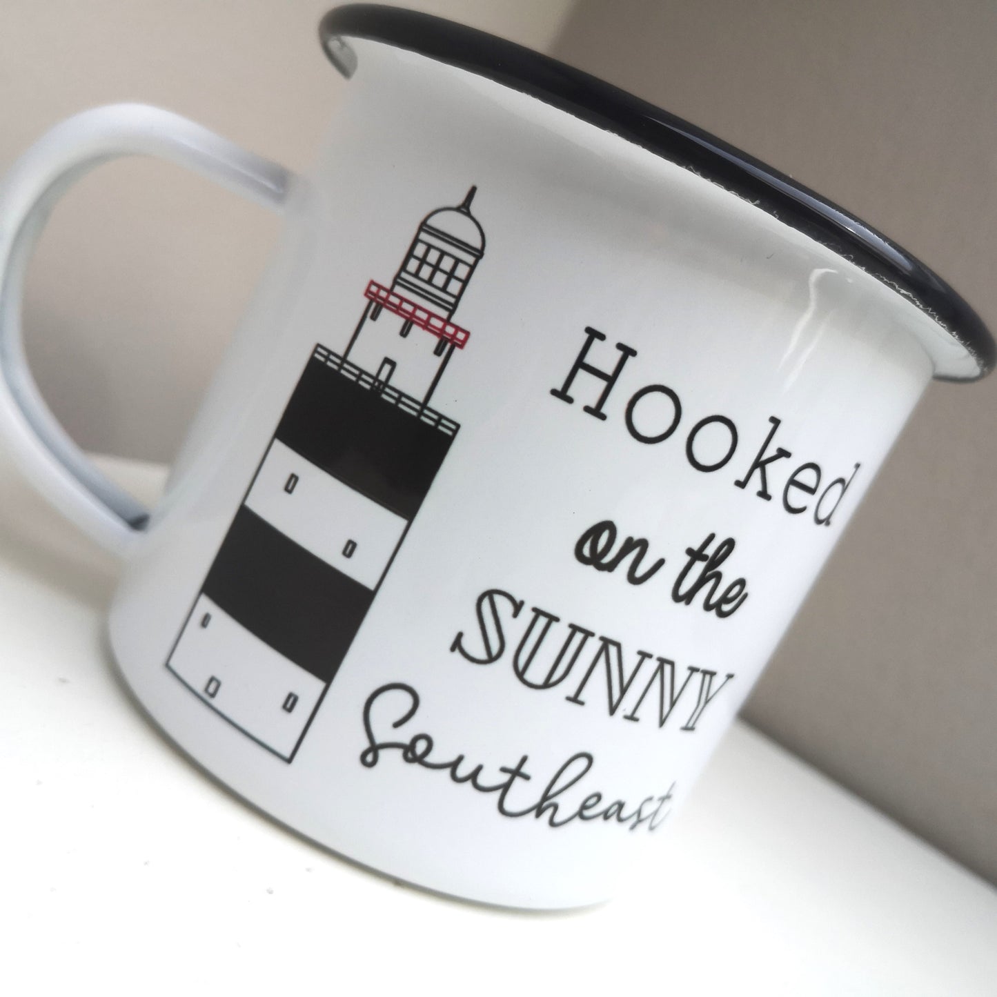 Close up of the Hooked on the Sunny Southeast enamel mug, with a drawing of the infamous Hook Head lighthouse on it