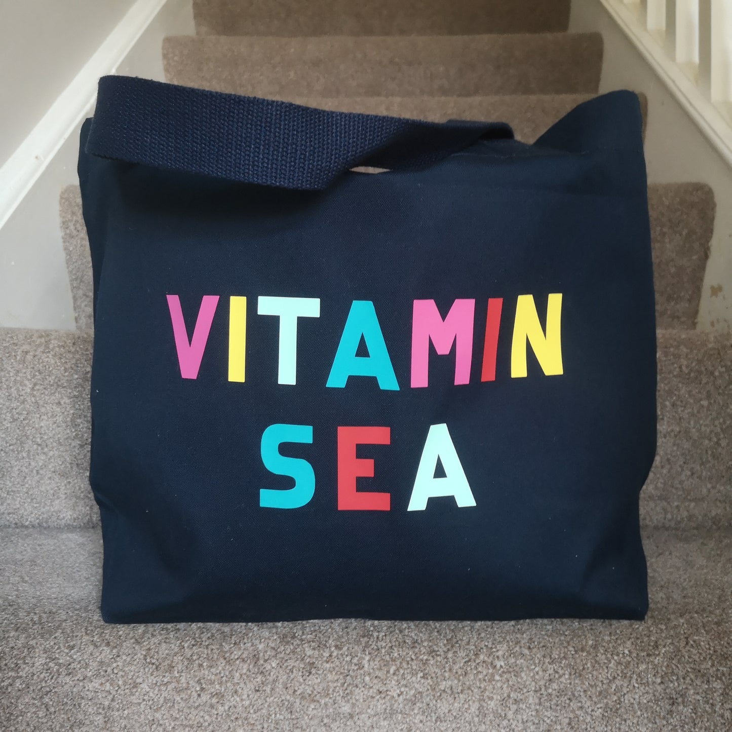 A navy organic cotton tote with toggle closing with VITAMIN SEA in different coloured bright lettering on the front
