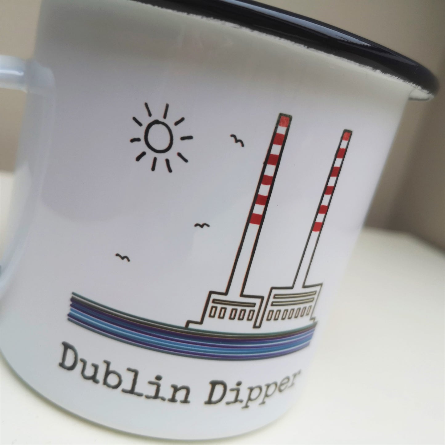 A close up of a white steel enamel mug with the poolbeg towers on it, with DUBLIN DIPPER written in type font below
