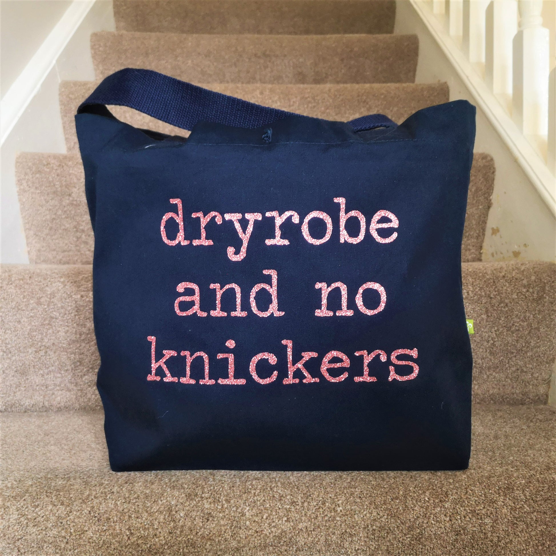 A navy organic cotton tote with toggle closing, with the following slogan written in type font on the front in sparkly rose gold glitter - Dryobe and no knickers