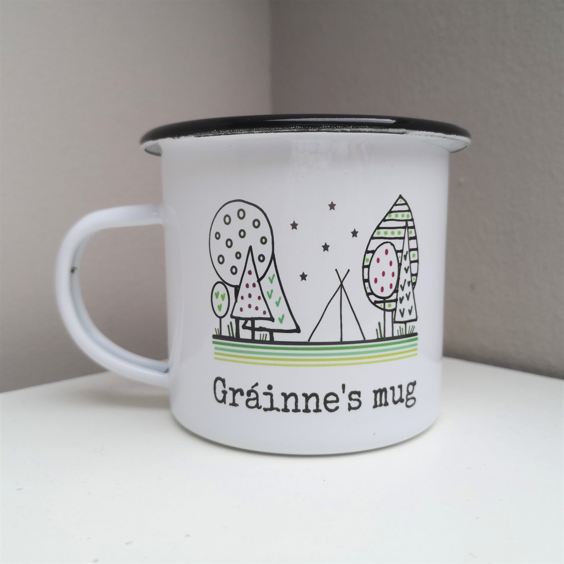 A White enamel mug with a black rim with the following on the front - a hand drawn forest scene with a tent below starry skies, and a personalised message underneath