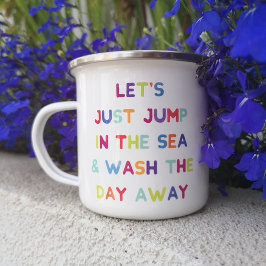 A white steel enamel mug with a stainless steel rim, with the following rainbow coloured message on it - LET'S JUST JUMP IN THE SEA AND WASH THE DAY AWAY