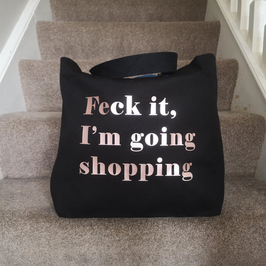 A black organic cotton tote with toggle closing with the following written on the front in rose gold type font - FECK IT, I'M GOING SHOPPING