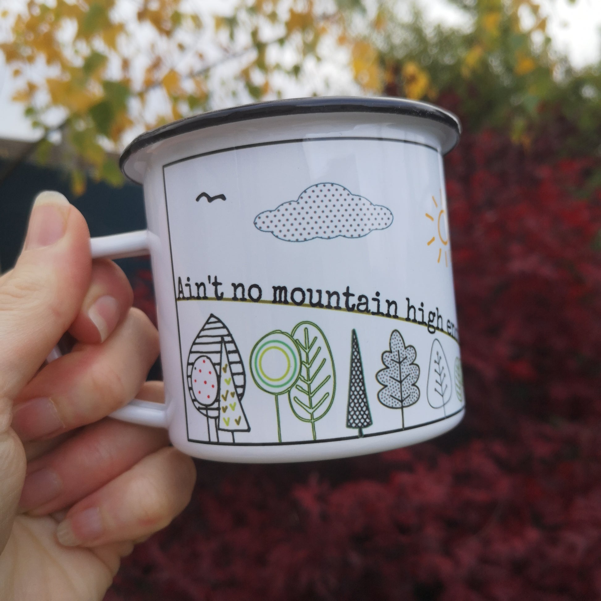 A steel enamel cup with a mountain scene on it with various trees and the following text running along the mountain ridge - Ain't no mountain high enough to keep me from seeing that view