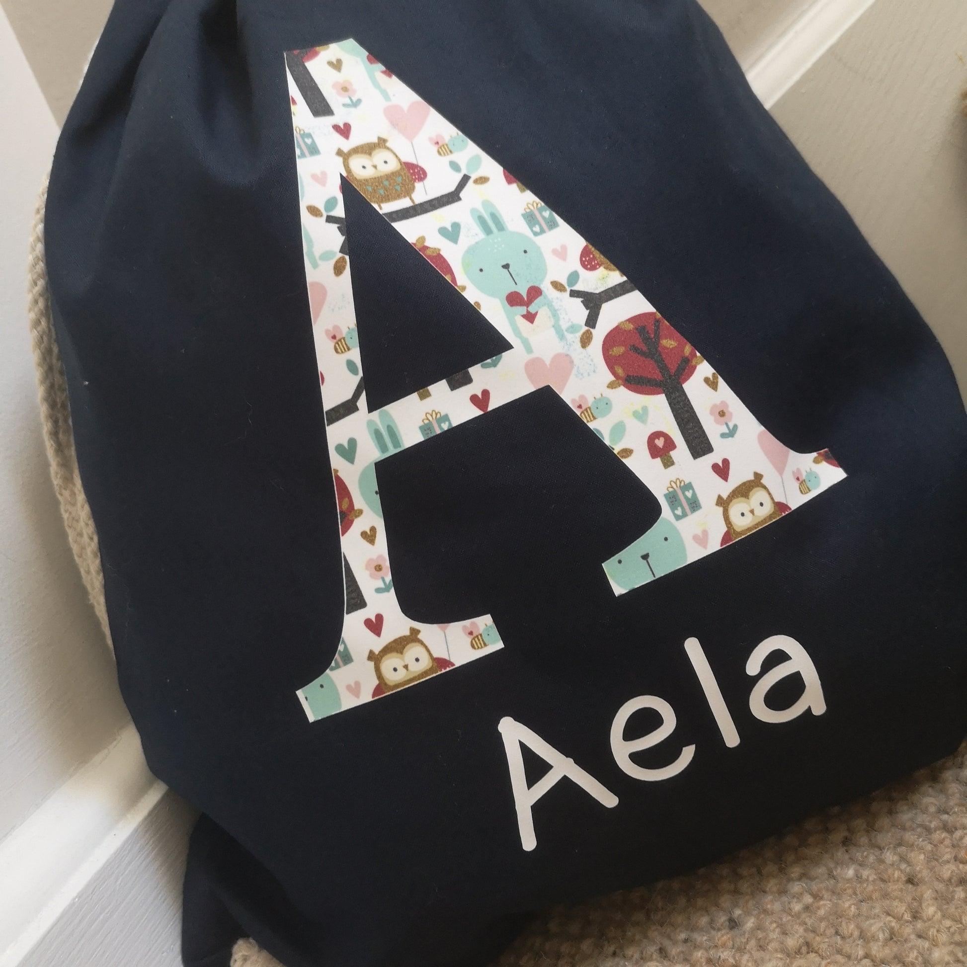 A close up of a royal navy personalised light drawstring bag with a patterned Initial and their name underneath