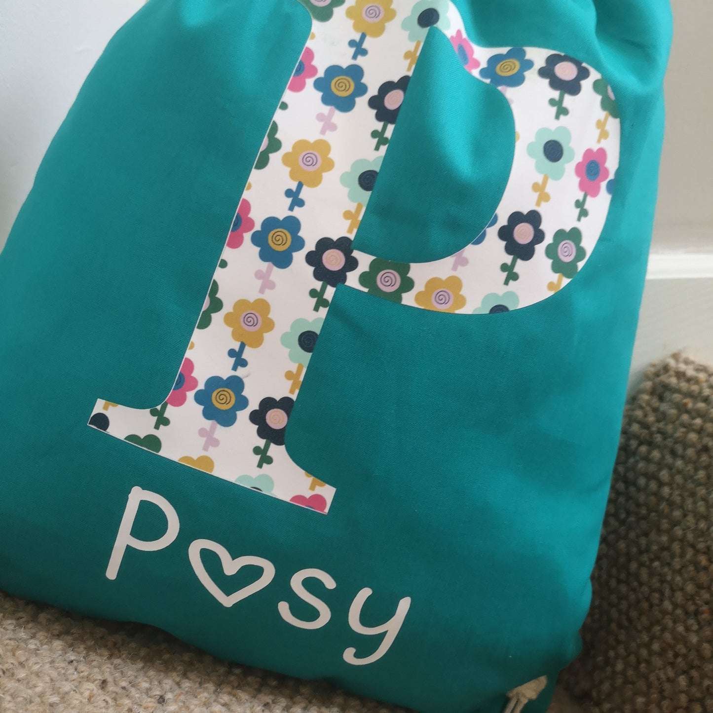 A close up of an emerald green personalised light drawstring bag with a patterned Initial and their name underneath