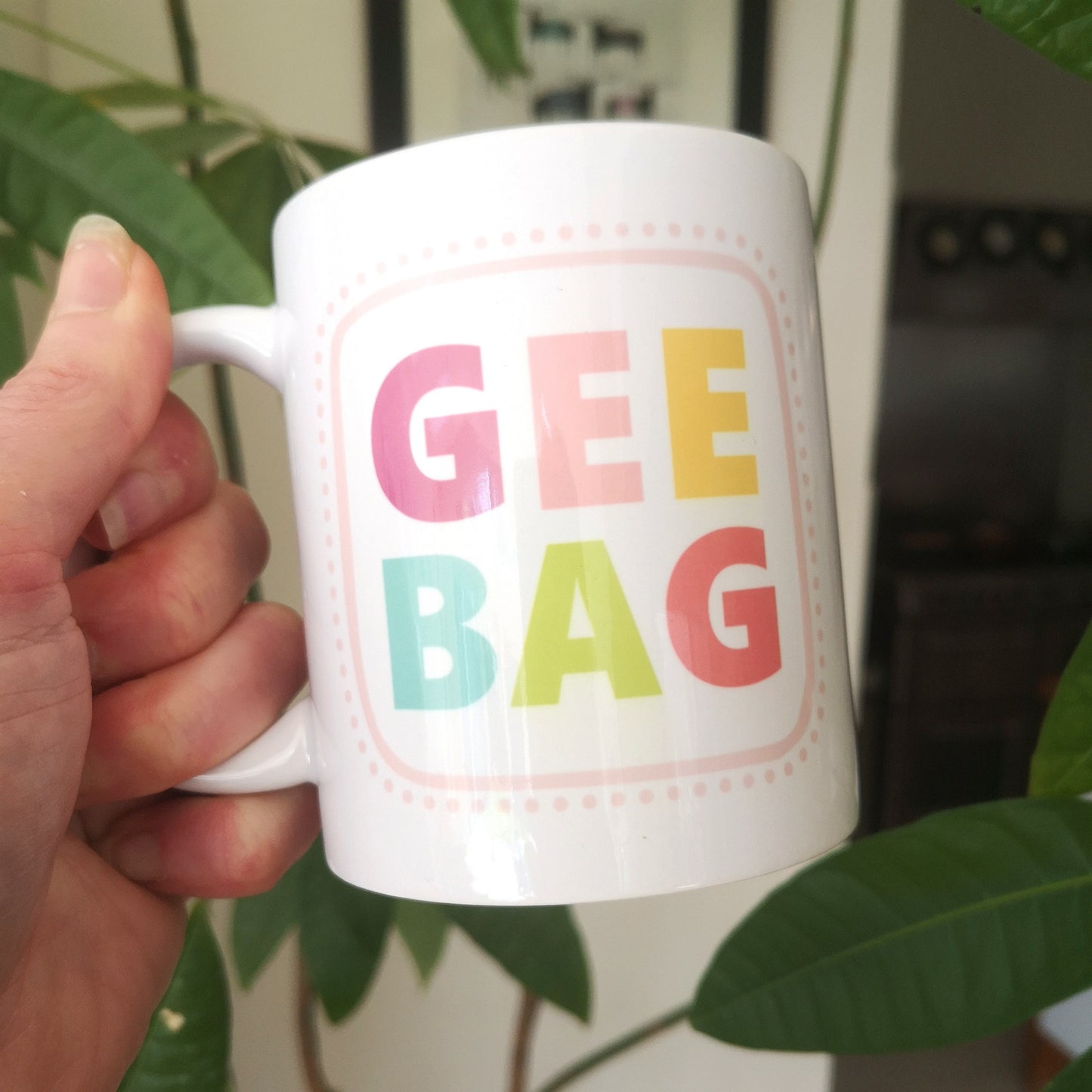 A white ceramic mug with GEEBAG written on the fron tin pastel lettering and spotty borders in pink