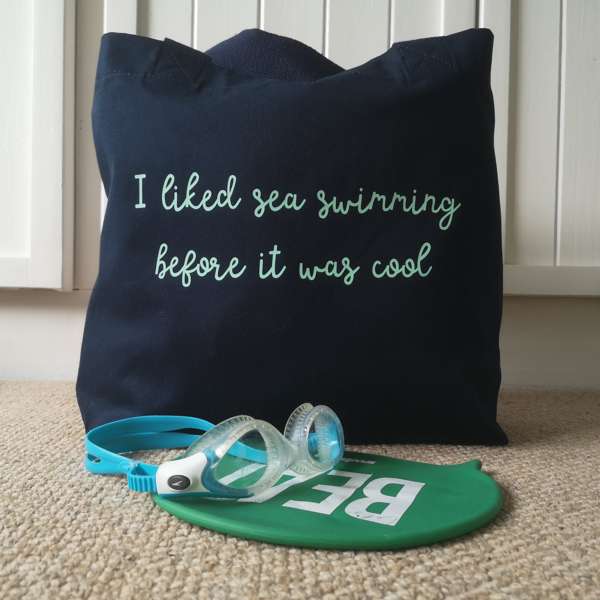 A navy organic cotton tote with toggle closing with the following text on the front in mint green handwrittenfont - I liked sea swimming before it was cool