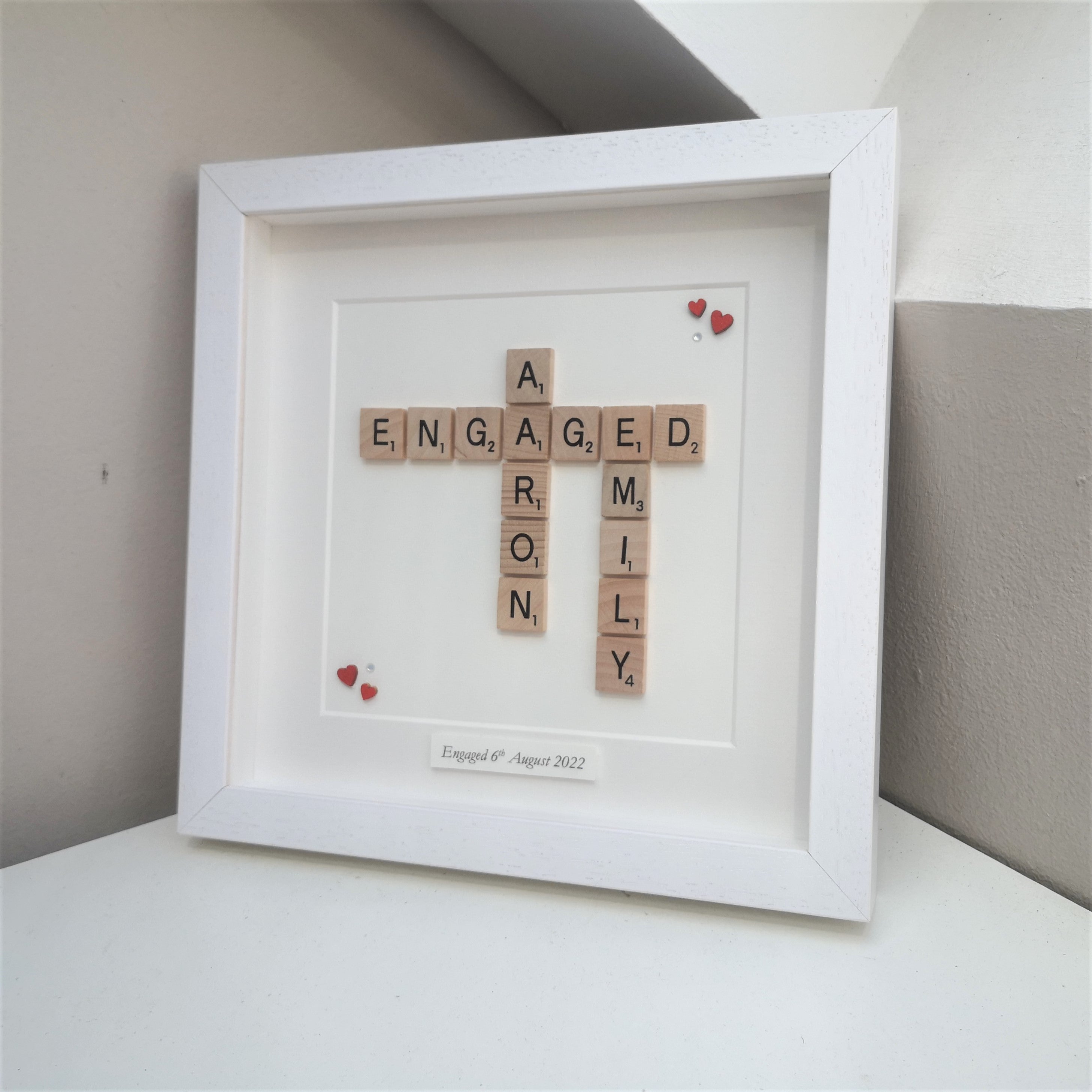 Personalised Engagement Scrabble name frame with wooden red hearts in the corner on a white background