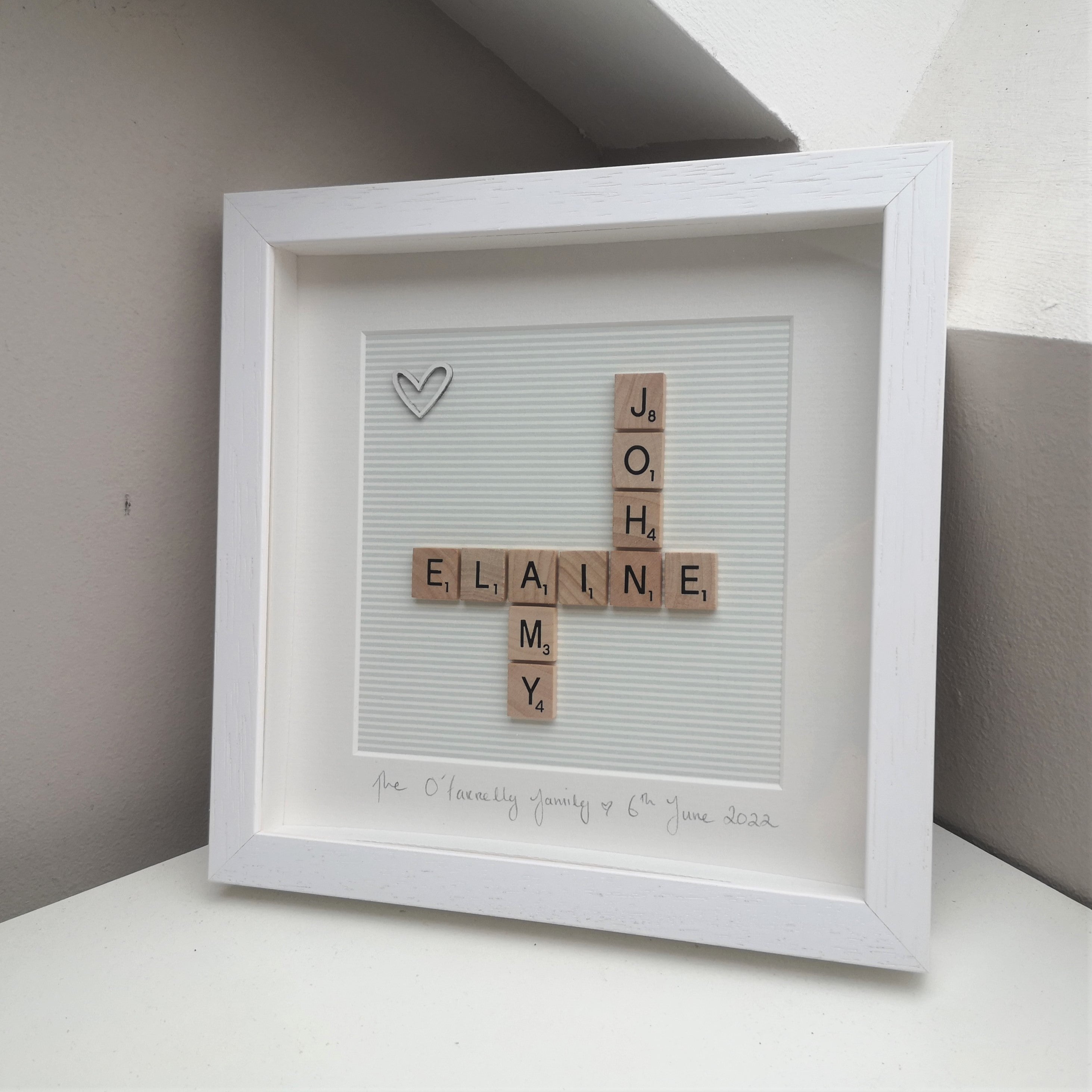 Personalised Couples Scrabble name frame with wooden white heart in the corner on a striped grey backing