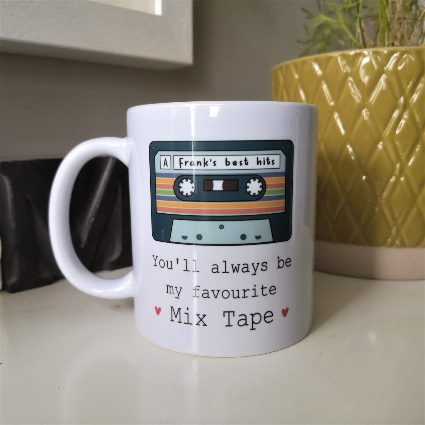 A white ceramic mug with a picture of an old cassette tape with a personalised message written on it, then underneath the tap is 'You'll always be my favourite mix tape' with 2 red hearts either side of it
