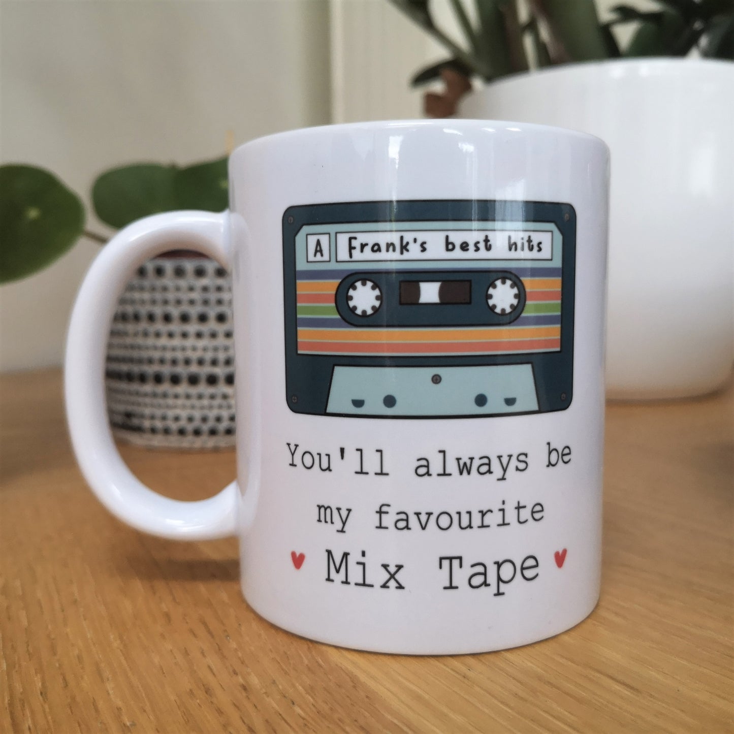 A white ceramic mug with a picture of an old cassette tape with a personalised message written on it, then underneath the tap is 'You'll always be my favourite mix tape' with 2 red hearts either side of it