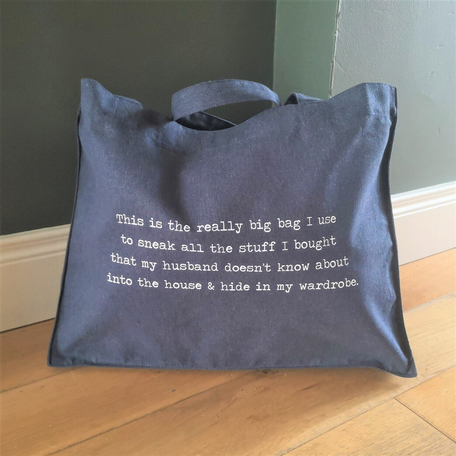 Another view of a large midnight blue organic cotton tote with the following text on it - This is the really big bag I use to sneak all the stuff I bought that my husband doesn't know about into the house & hide in my wardrobe.