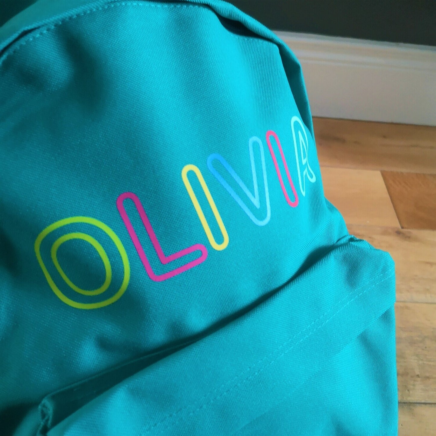 A close up of an emerald green kids backpack with their name written along the top in different coloured letters