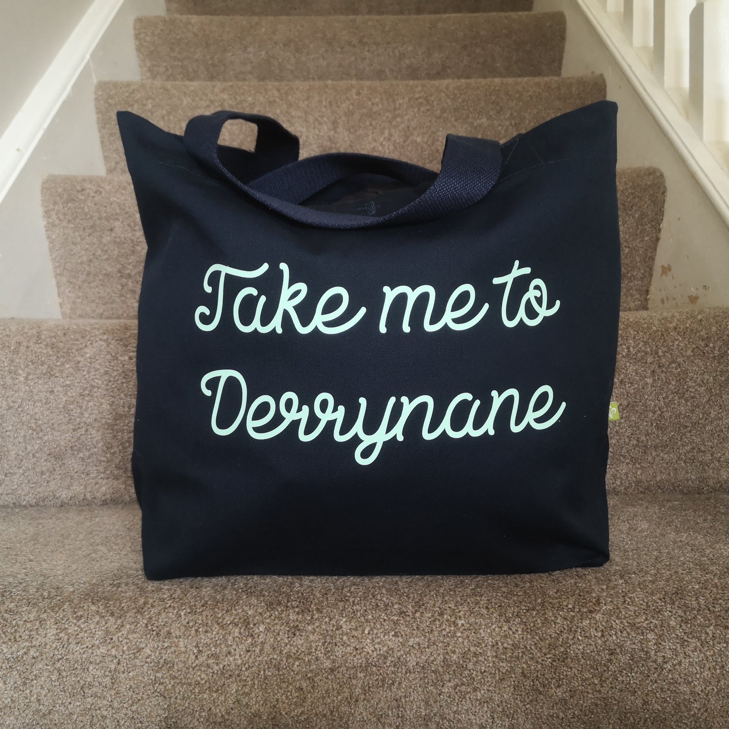 A black organic cotton tote with toggle closing with the following text on the front in white type font - Take me to (your choice of text here)